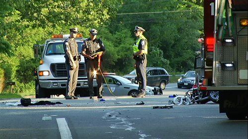 Police officers and firefighters at the scene of a vehicle accident with debris on the road.